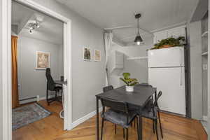Dining space with light wood finished floors, stacked washer and clothes dryer, a baseboard heating unit, and an office area