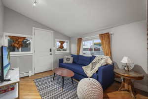 Living area with lofted ceiling, light wood-type flooring, and baseboard heating