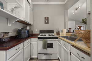 Kitchen featuring white range with gas stovetop, white cabinets, dark countertops, light tile patterned floors, and lofted ceiling