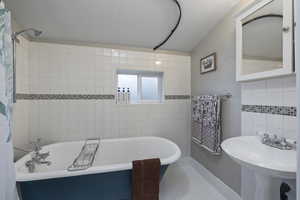 Full bath featuring tile walls, a textured ceiling, tile patterned flooring, and a combined bath / shower with freestanding tub