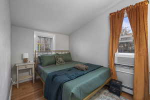Bedroom with wood finished floors, a textured wall, lofted ceiling, a baseboard radiator, and cooling unit