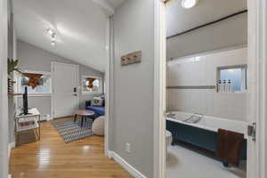 Bathroom with bathing tub / shower combination, a textured wall, vaulted ceiling, and light wood finished floors