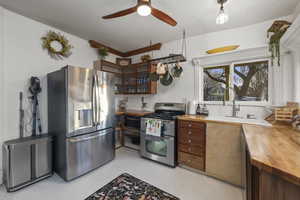 Kitchen featuring wood counters, appliances with stainless steel finishes, glass insert cabinets, a textured ceiling, and a ceiling fan
