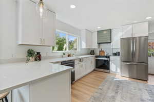 Kitchen with stainless steel appliances, white cabinetry, hood vent, light stone countertops, and light wood finished floors