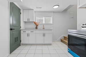 Kitchen featuring stainless steel electric stove, a textured ceiling, light countertops, white cabinetry, and light tile patterned floors