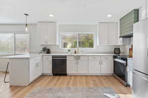 Kitchen featuring a peninsula, white cabinets, stainless steel appliances, wall chimney exhaust hood, and pendant lighting