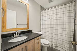 Full bathroom with vanity, shower / bathtub combination with curtain, and a textured ceiling