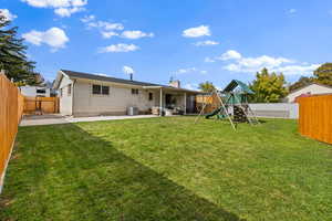 Rear view of property with a fenced backyard, a patio, a playground, brick siding, and a chimney