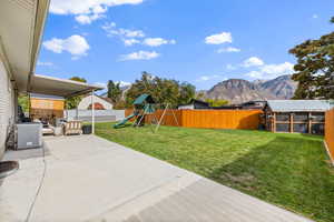 Fenced backyard featuring a mountain view, a playground, a patio area, and an outbuilding
