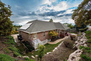View of home's exterior with a wooden deck, solar panels, brick siding, and roof with shingles
