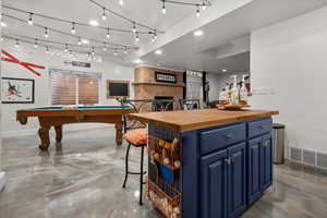 Game room featuring concrete floors, pool table, a bar, and a brick fireplace