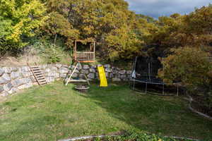 View of green lawn with a trampoline, a playground, and an outdoor fire pit