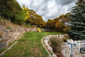 View of green lawn featuring a playground and a trampoline