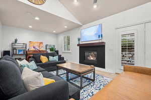 Living room with lofted ceiling, recessed lighting, light wood finished floors, and a glass covered fireplace