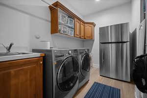 Laundry room with light wood-type flooring, washer and clothes dryer, and cabinet space