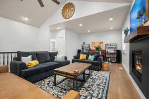 Living room featuring a glass covered fireplace, recessed lighting, high vaulted ceiling, wood finished floors, and ceiling fan
