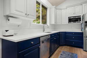 Kitchen with blue cabinetry, white cabinets, stainless steel appliances, light wood-style floors, and lofted ceiling