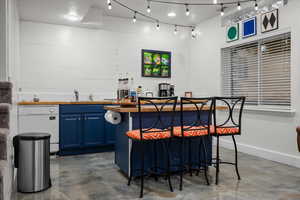 Kitchen with blue cabinets, butcher block countertops, dishwasher, and concrete flooring