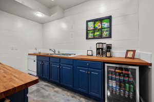 Indoor wet bar with wood counters, blue cabinets, concrete flooring, white dishwasher, and beverage cooler