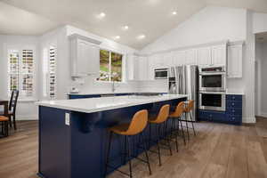 Kitchen with blue cabinetry, white cabinetry, light wood-style flooring, appliances with stainless steel finishes, and a kitchen island