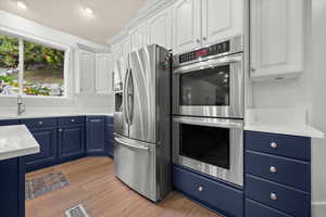 Kitchen featuring blue cabinetry, stainless steel appliances, white cabinetry, light stone counters, and light wood-type flooring