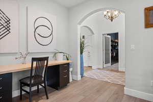 Home office with light wood finished floors, arched walkways, and a chandelier