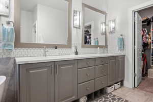 Bathroom featuring a walk in closet, tasteful backsplash, double vanity, and light tile patterned floors