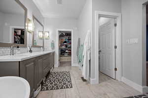 Full bath featuring a spacious closet, double vanity, backsplash, baseboard heating, and light tile patterned flooring