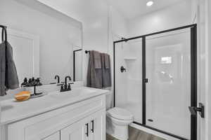 Bathroom featuring a shower stall, vanity, dark wood finished floors, and recessed lighting