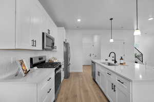 Kitchen featuring appliances with stainless steel finishes, white cabinets, a center island with sink, decorative light fixtures, and light stone countertops