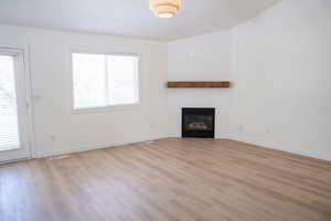 Unfurnished living room with a glass covered fireplace and light wood-style flooring