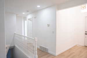 Corridor with an upstairs landing, light wood-type flooring, and recessed lighting
