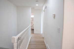 Hallway featuring an upstairs landing, light wood-style floors, and recessed lighting