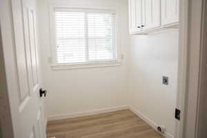 Washroom with hookup for an electric dryer, cabinet space, and light wood finished floors