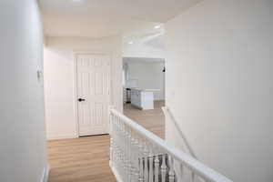 Corridor featuring an upstairs landing, light wood finished floors, vaulted ceiling, and recessed lighting