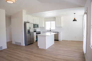 Kitchen featuring appliances with stainless steel finishes, white cabinetry, a center island, decorative backsplash, and pendant lighting