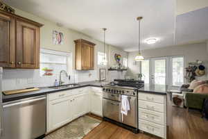 Kitchen featuring a peninsula, appliances with stainless steel finishes, dark wood-type flooring, decorative light fixtures, and backsplash