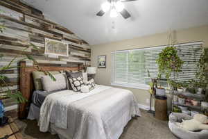 Carpeted bedroom with wooden walls, lofted ceiling, ceiling fan, and a textured ceiling