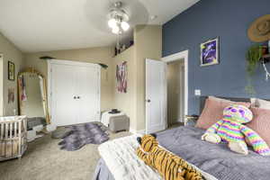 Carpeted bedroom featuring vaulted ceiling, a ceiling fan, and a closet