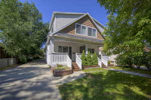 Bungalow with covered porch, a front lawn, roof with shingles, and driveway