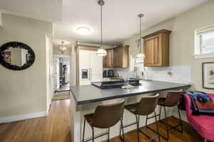 Kitchen featuring dark countertops, brown cabinets, a peninsula, a kitchen breakfast bar, and decorative light fixtures