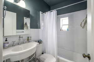 Bathroom featuring shower / bath combo, tile walls, and a wainscoted wall