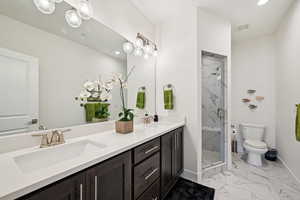 Full bath featuring double vanity, light marble finish flooring, a marble finish shower, and recessed lighting