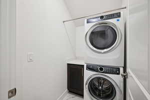 Laundry room with estacked washer and dryer, light marble finish floors, and cabinet space
