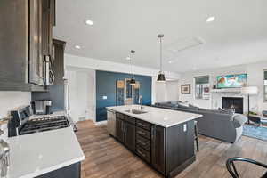 Kitchen with dark brown cabinets, pendant lighting, appliances with stainless steel finishes, open floor plan, and an island with sink