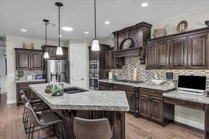 Kitchen with dark brown cabinetry, decorative light fixtures, stainless steel appliances, decorative backsplash, and dark wood-style flooring