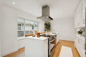 Kitchen with electric range, light wood-style floors, white cabinetry, island range hood, and recessed lighting