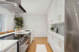 Kitchen with stainless steel appliances, under cabinet range hood, white cabinetry, light wood finished floors, and recessed lighting