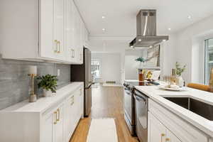 Kitchen with white cabinetry, light wood-type flooring, island exhaust hood, light stone countertops, and tasteful backsplash
