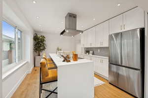 Kitchen featuring freestanding refrigerator, white cabinets, a kitchen breakfast bar, light wood finished floors, and tasteful backsplash